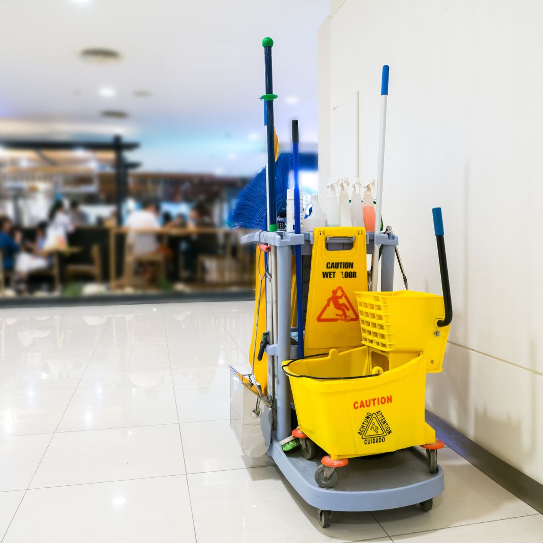 A fully equipped gray cleaning cart with mops, brooms, spray bottles, and yellow 